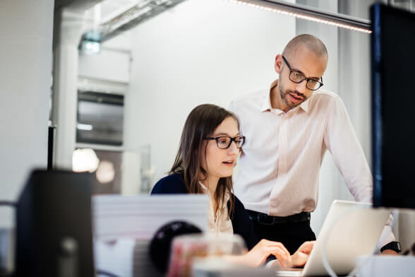 Business man looking at his coworker's computer screen to work on podcast